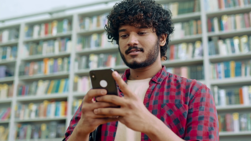 Happy indian or arabian millennial guy, freelancer or student, using his smartphone, chatting with friends on social networks, texting sms, browses internet,smile friendly. Wireless technology Royalty-Free Stock Footage #1093653371