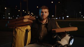A smiling delivery man sits on a scooter with pizza boxes and looks at the camera. Video without noise and artefacts