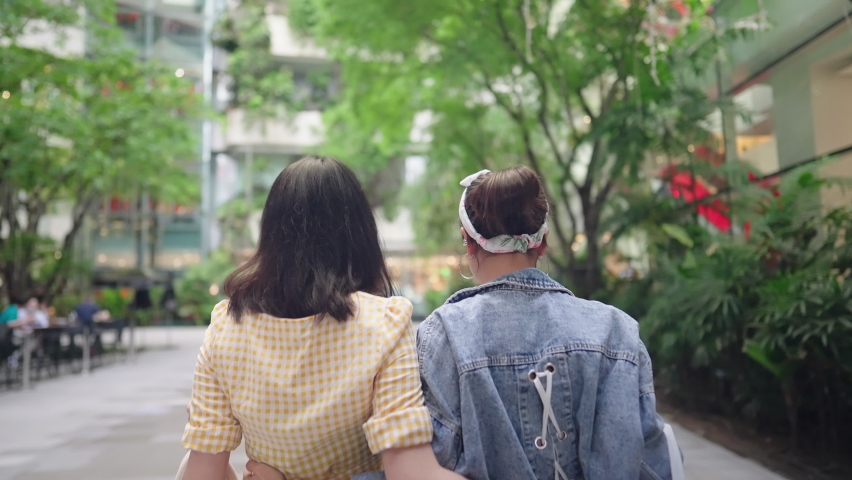 Two Asian girlfriends walking with shopping bags inside downtown shopping area, Reopening Business After Covid-19. Modern Urban Community Mall. credit card top spender, City Woman Lifestyle, rear view