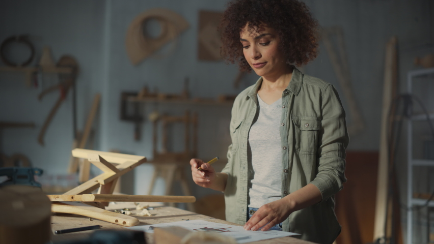Young Stylish Female Carpenter Assembling a Wooden Chair. Professional Furniture Designer Working in a Studio in Loft Space with Tools on Walls. Handheld Shot.