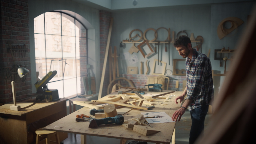 Young Artisan Furniture Designer Marking Out Dimensions on a Blueprint and Starting to Assemble a Wooden Chair. Talented Carpenter Working in a Studio in Loft Space with Tools on the Walls.