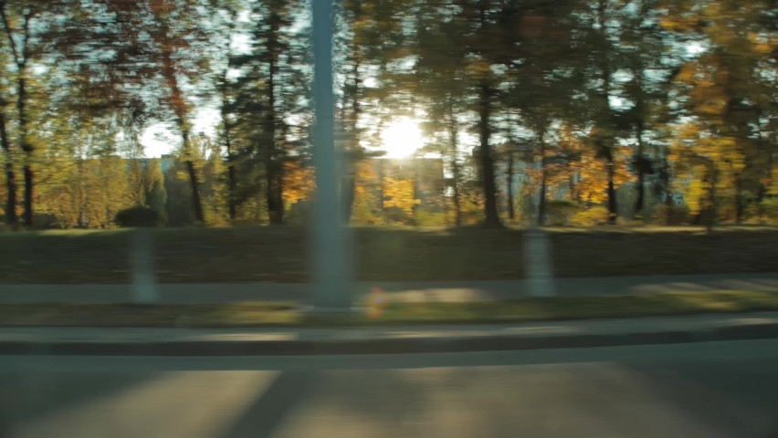 Sunlight shines through autumn trees in city town. View through side car auto window in motion. Multi-storey residential buildings on background. Tourism and travel in fall, journey trip concept Royalty-Free Stock Footage #1093667689