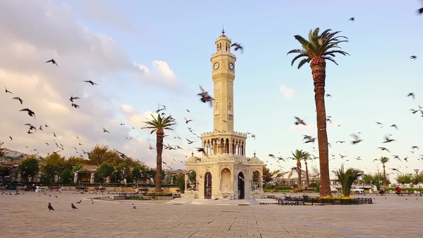 Flock of pigeons flying around the Izmir Clock Tower at the Konak Square during sunset in Izmir, Turkey. Slow motion Royalty-Free Stock Footage #1093668625