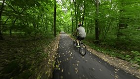 Man in a protective helmet is riding a bicycle along an asphalt path in the forest.