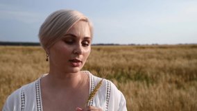 Close-up portrait of beautiful blond short haired caucasian woman holding ear of wheat on agricultural wheat field in a sunny day. Selective focus. Real time video. Beautiful people theme.