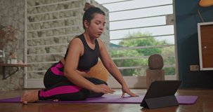 Girl practicing yoga on her mat and watching class with teacher online via tablet. Girl stretching body at home. Health concept