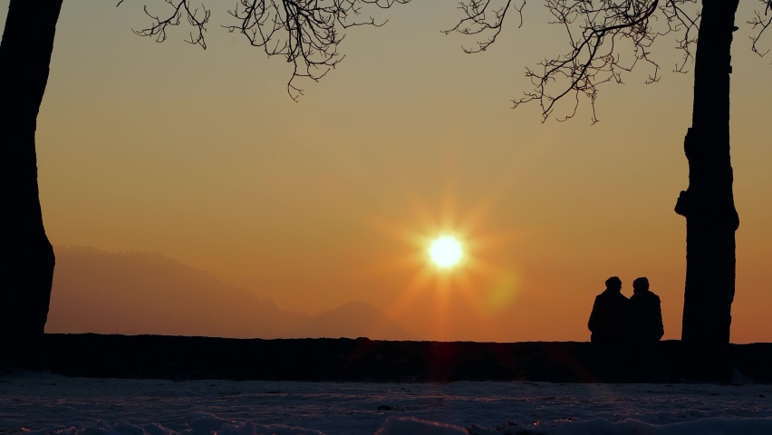 Footage of a couple sitting on a wall and observing a beautifull sunset