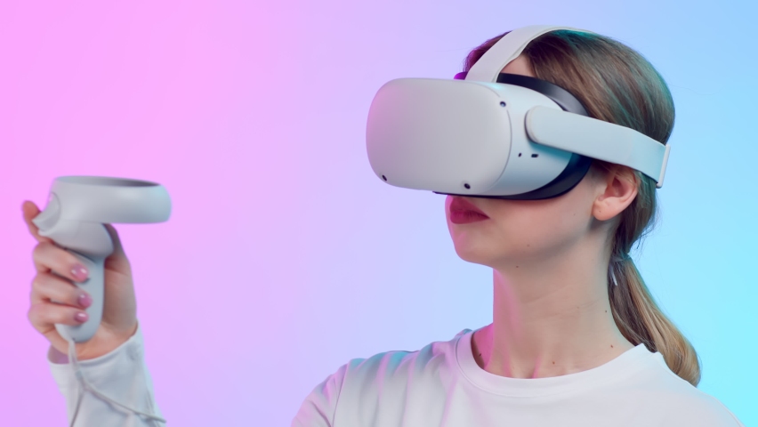 Close up of young woman in vr goggle moving hand with controller isolated over neon background. Female play video game in augmented reality glasses Royalty-Free Stock Footage #1093695625