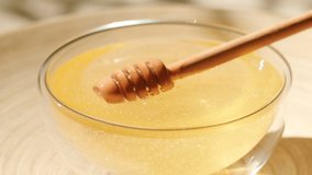 Honey dripping, pouring from honey dipper in a glass bowl. Close-up. Organic Thick honey dipping from the wooden honey spoon, closeup. 4K UHD video footage. Slow motion