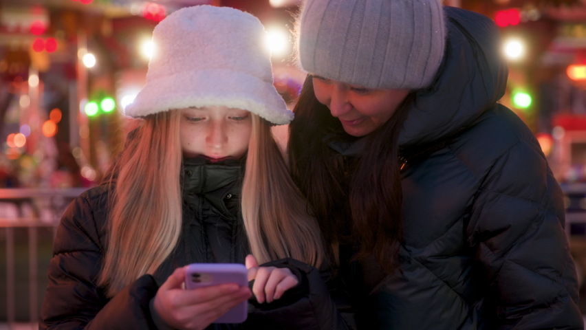 Friends looking at smart phone together. Dolly shot of teenage females socializing on cellphone. They are spending leisure time during winter night. High quality 4k footage