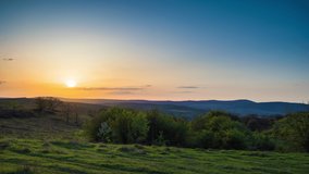 A large spring flowering field with bright yellow small plants in a mountain and meadow valley against the backdrop of a golden evening sunset sky, in warm country of Bulgaria. 4K UHD timelapse