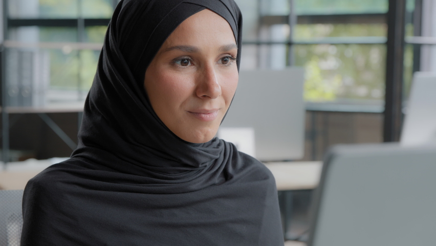 Close-up positive young woman office worker professional manager working on computer successful attractive arab businesswoman in hijab sitting at workplace looking at camera smiling enjoying Royalty-Free Stock Footage #1093707995