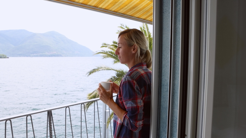 Young woman having a cup of tea on her balcony with lake view