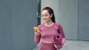 Smiling fit young woman using cell phone checking fitness applications standing on urban grey wall background outdoors. Online gym free exercises, sport and health care commercial apps concept. - Powered by Shutterstock - Get 15% off with code: PIKWIZARD15