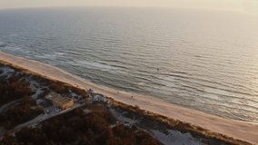 Bird's-eye view, a group of people stand on a sandy beach washed by foamy waves and look into the sea distance. Video from a drone on a sunny day.