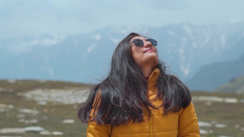 Portrait of teenager Indian girl tourist with sunglasses looking at snow covered mountains in Manali, Himachal Pradesh, India. Travel lifestyle. Female travel influencer enjoying vacation in mountains | Shutterstock HD Video #1093722053