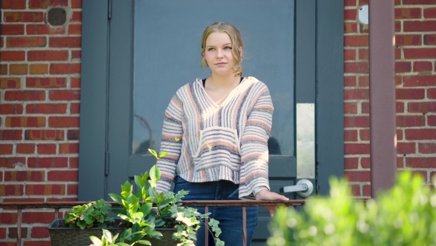 Girl standing against rail outside of a school door. Slow motion.