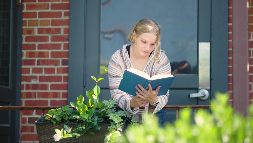 Girl student reading book over a side rail outside of a door. Slow motion. Royalty-Free Stock Footage #1093723181