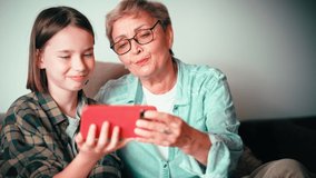 Happy grandmother and her granddaughter spending time together watching videos on a cellphone. A senior woman and a child girl are having fun.