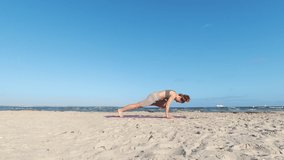 4k slow motion video of a girl doing morning yoga routine  at the beach of Baltic sea over clear blue sky