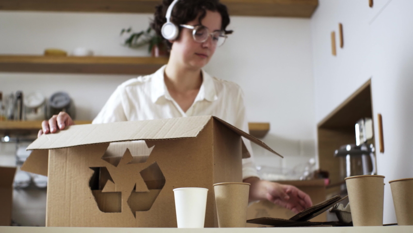 Young active woman dances in white headphones listens to music stacking sorted garbage from cardboard materials for recycling and disposal. Recycling of disposable products
 Royalty-Free Stock Footage #1093731965
