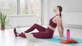 fitness online. a woman in a burgundy tracksuit with laptop on a mat in a gym. Record video and online lessons for sports. clothes and shoes for gymnastics. professional trainer. 