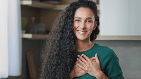Young curly girl hispanic frank honest woman stand indoor put folded palms on chest make thankful trust gesture demonstrate belief friendly sign sincere apology devotion tenderness and charity - Powered by Shutterstock - Get 15% off with code: PIKWIZARD15