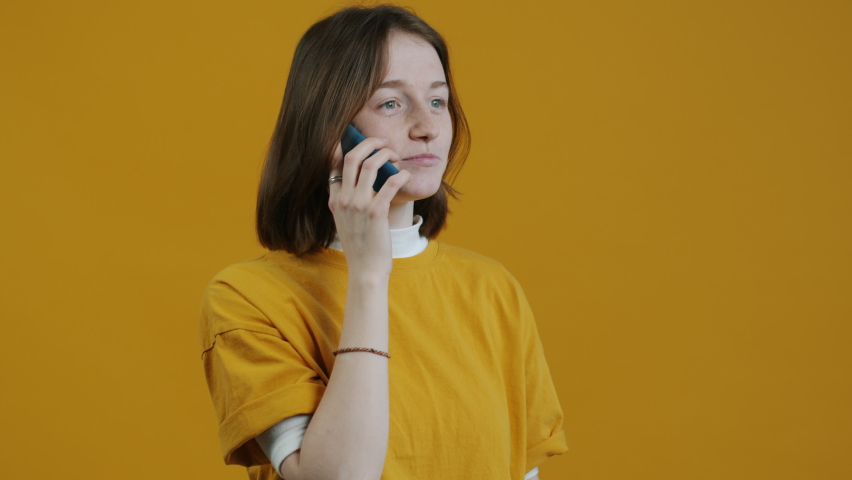 Portrait of happy young woman talking on mobile phone and smiling enjoying communication on yellow background. People and modern technology concept. Royalty-Free Stock Footage #1093737821