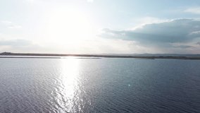 Boundless calm Black Sea with cool water reflecting light extends beyond the horizon, under colored sky with white volatile clouds and a bright dawn warm spring sun. UHD 4K video realtime