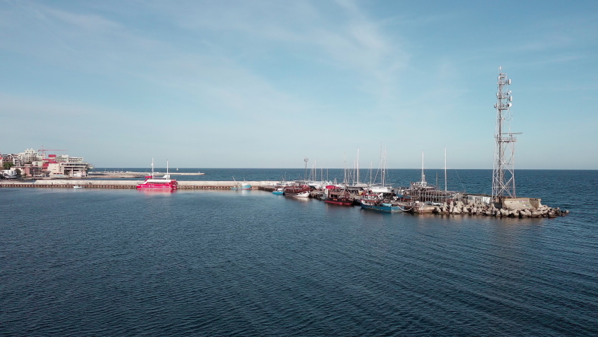 A small sea fishing port with boats in the calm deep cool Black Sea adjoins the ancient resort small town of Pomorie in Bulgaria, under a blue cloudy sky. UHD 4K video realtime