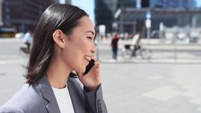 Young happy busy professional Asian business woman executive wearing suit making call on cellular holding smartphone talking on mobile phone having chat on cellphone walking on urban city street. - Powered by Shutterstock - Get 15% off with code: PIKWIZARD15