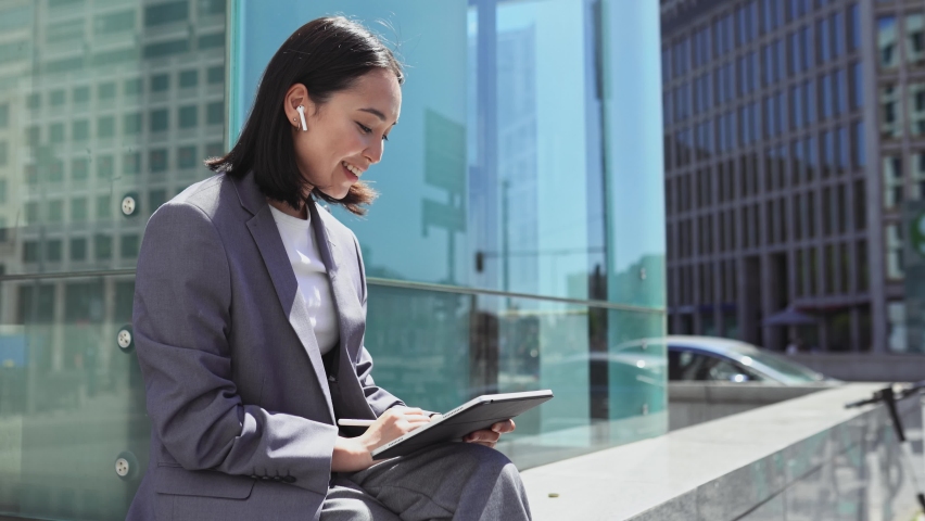 Asian elegant professional business woman wearing suit using digital tablet outside office, happy businesswoman executive holding pad corporate technology device on city street glass background. Royalty-Free Stock Footage #1093742113