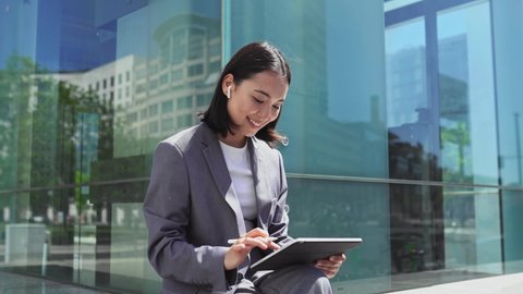 Asian elegant professional business woman wearing suit using digital tablet outside office, happy businesswoman executive holding pad corporate technology device on city street glass background. 스톡 비디오