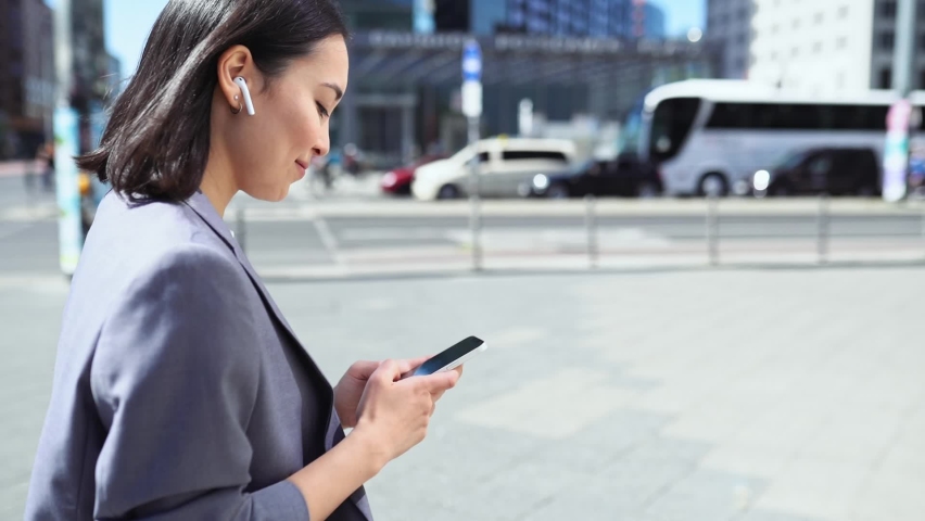 Young Asian business woman wearing suit using smartphone walking in big city on street outdoor. Korean lady professional executive typing on cellular phone, online mobile technology business apps Royalty-Free Stock Footage #1093742133