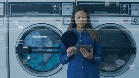 Composite video of biracial young woman using tablet pc at laundromat and communication icons. Technology, convenience, laundry, graphic, lifestyle, connection, networking, global communications. - Powered by Shutterstock - Get 15% off with code: PIKWIZARD15