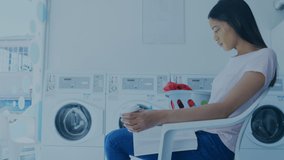 Video of biracial young woman working while waiting at laundromat with clock and cloud icons. Digital composite, convenience, laundromat, connection, global communications, cloud computing, time. - Powered by Shutterstock - Get 15% off with code: PIKWIZARD15