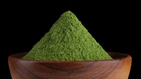 Matcha green tea powder in wooden bowl. Pouring green superfoods powder, close up