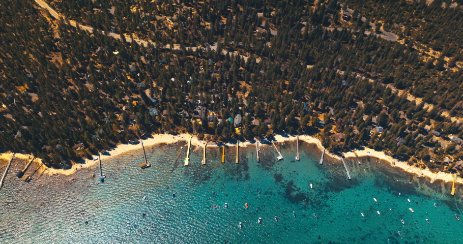 Clear blue waters of Lake Tahoe with boats sailing on. Wooded waterfront with numerous houses among the trees. Top view.