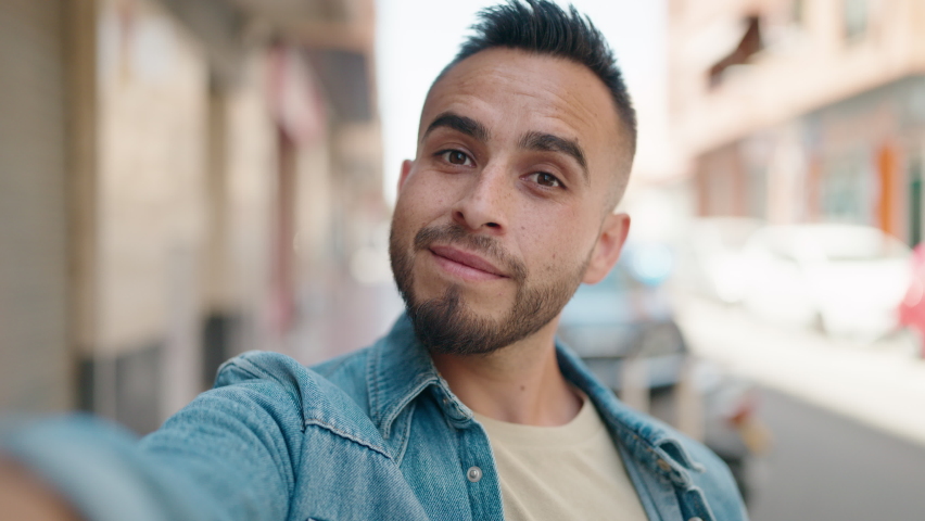 Young hispanic man smiling confident making selfie by the camera at street