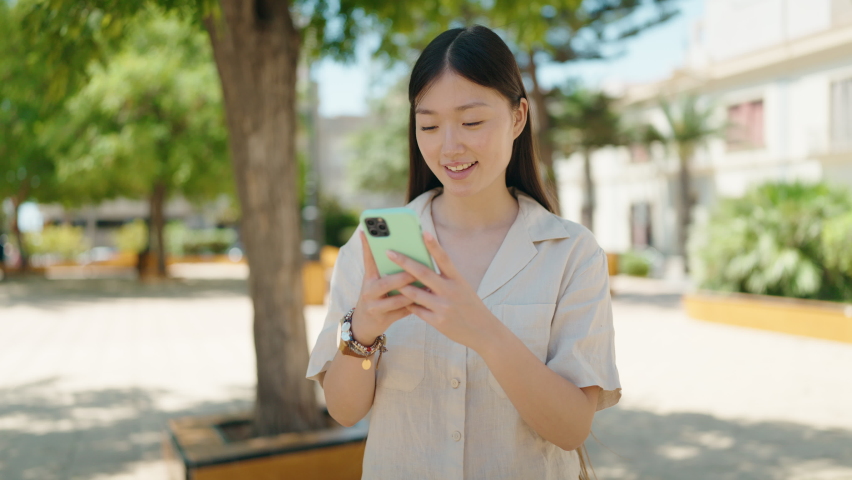 Chinese woman smiling confident using smartphone at park