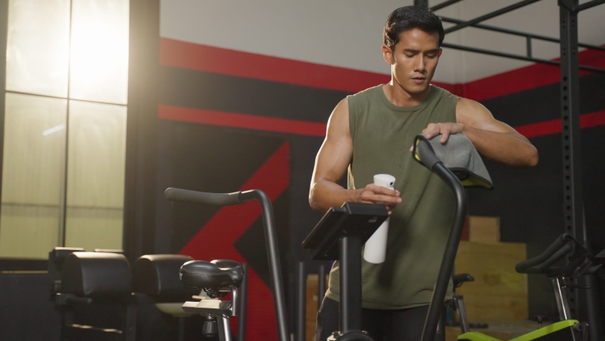 Asian handsome sportsman cleaning workout equipments in fitness club. Attractive young athlete man doing abs workout and excercise to building muscle for health care and wellness in gymnasium stadium.
