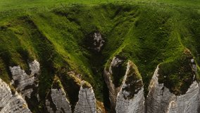View from above on the bizarre peaks of sheer cliffs, overgrown with dense bright grass. Drone video on a sunny day, Etretat, France