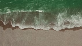 Top view of the sea shore. Emerald water with foam washes a shallow pebble beach, drone video.