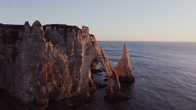Beautiful coastal cliffs of bizarre shapes with natural arches and wild beaches in the rays of the setting sun. Etretat, France, cliffs on the banks of the English Channel, drone video