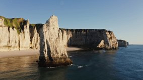 Snow-white cliffs with natural arches and a dense green cap of grass on top are washed by the waters of the English Channel. Drone video from the sea, Etretat, France