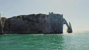 Picturesque coastal cliffs forming natural arches on the limestone coast of the English Channel. Etretat, France, drone video on a sunny summer day