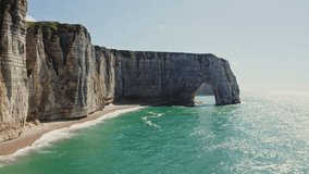 Alabaster sheer cliffs with a picturesque natural arch, washed by the waters of the English Channel. A deserted pebble beach at the foot of a cliff. Video from a drone. Etretat, France