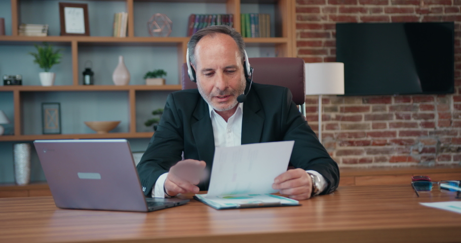 Workflow concept where likable confident purposeful adult bearded businessman in headset discussing financial report with business partners via videochat on laptop Royalty-Free Stock Footage #1093752701