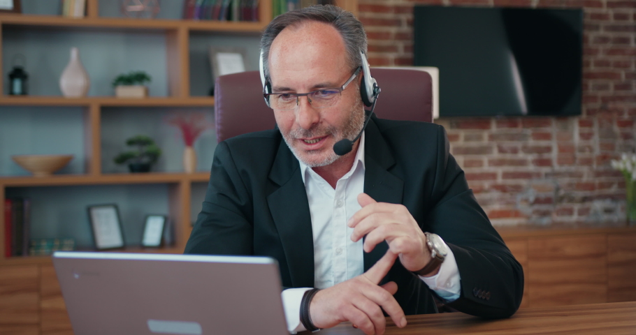 Good-looking confident successful skilled adult bearded businessman in wireless headset holding online meeting on laptop with business partners in office Royalty-Free Stock Footage #1093752723