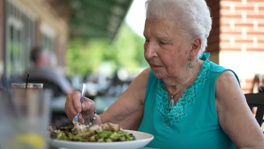 Closeup of elderly senior woman eating salad with fish chicken at an outdoor restaurant, cafe | Shutterstock HD Video #1093753965